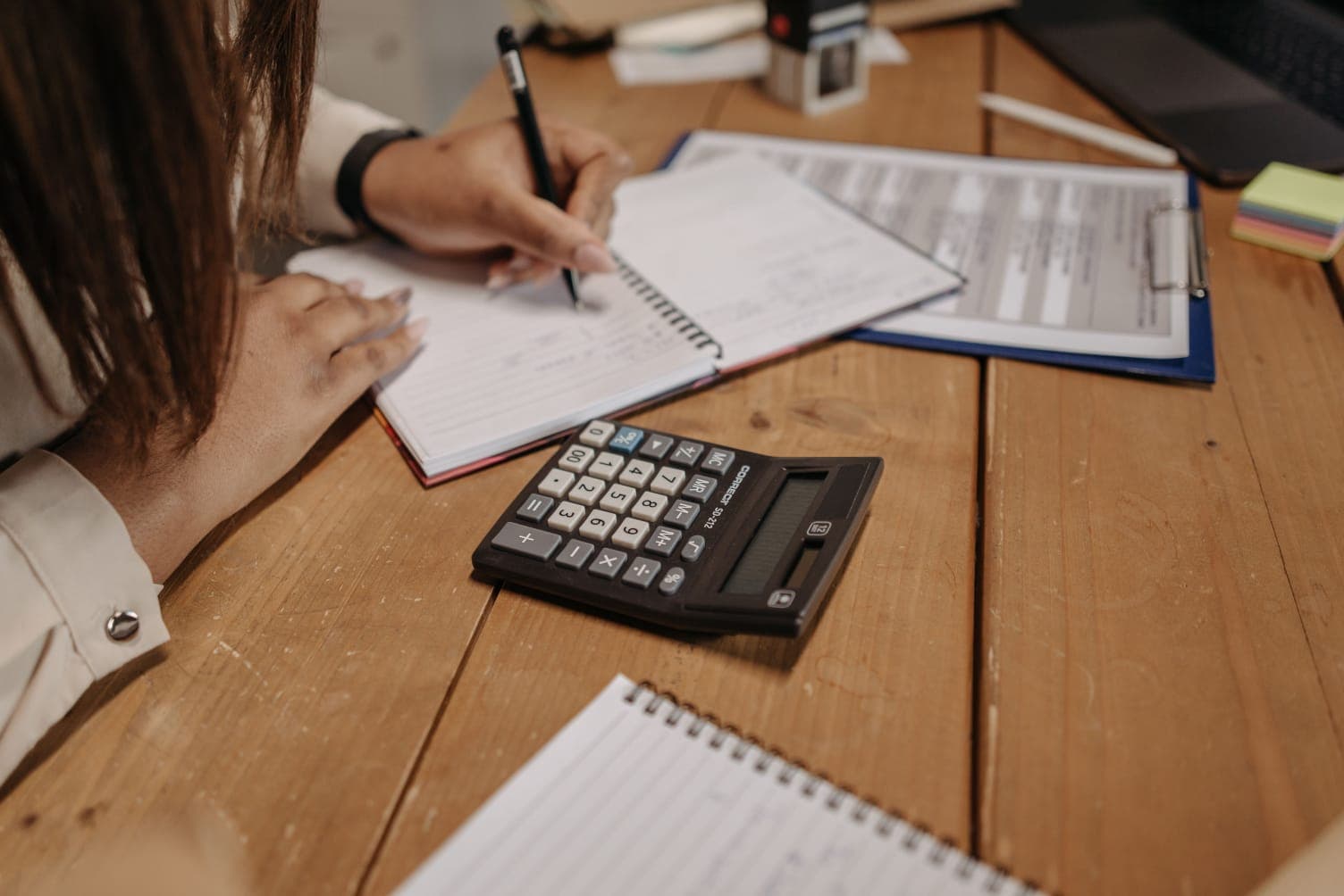 Contadora usando calculadora sobre relatório de índices contábeis e caderno de anotações