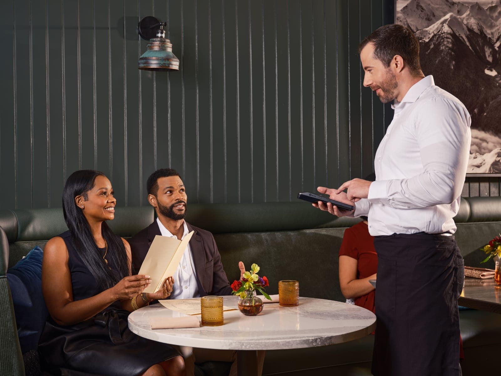 Garçom mostrando o cardápio em um tablet para o cliente na mesa do restaurante