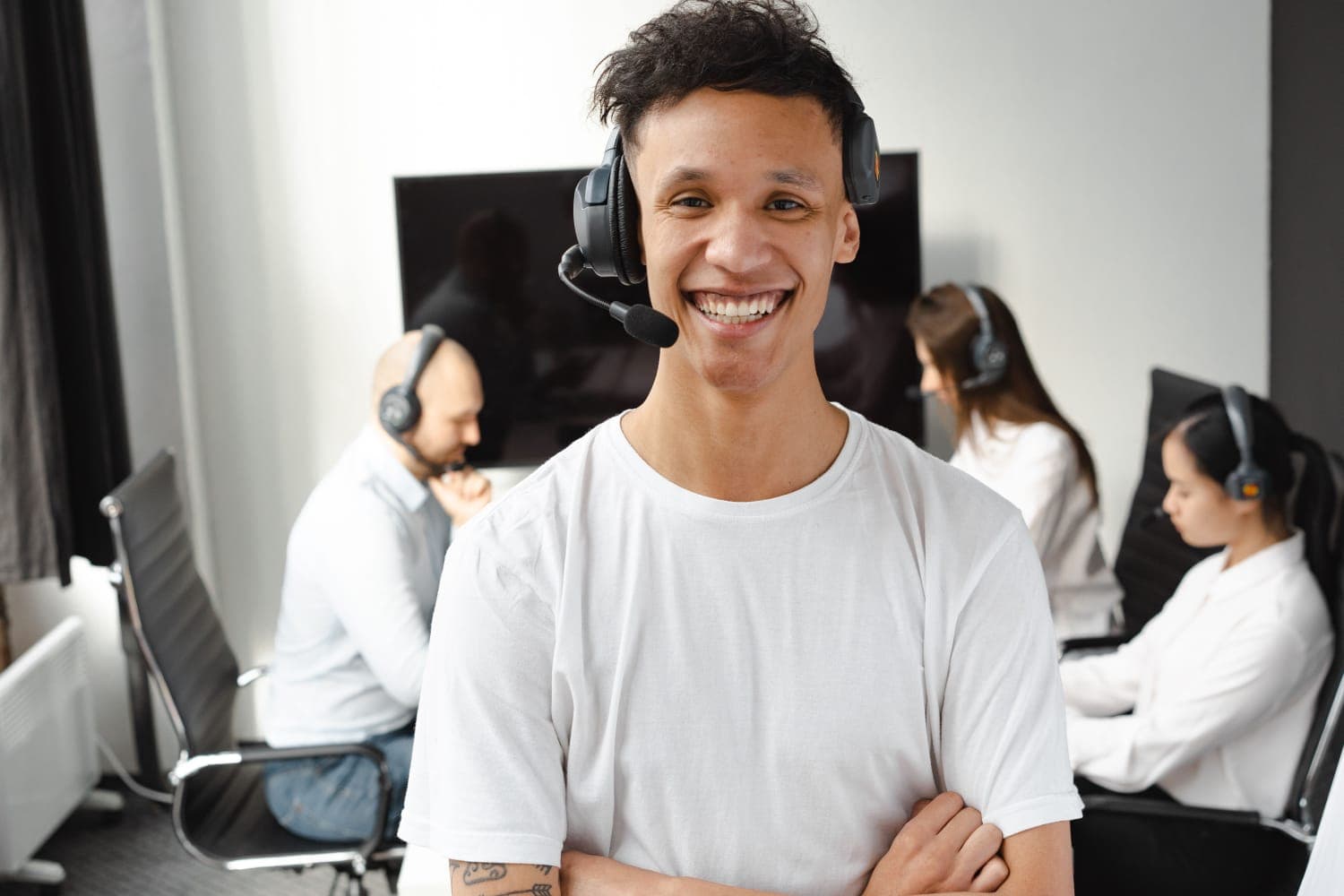 Atendente de suporte sorrindo com headset, com a equipe ao fundo